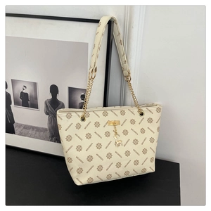 Detail of monogram tote bag with gold chain strap and deer charm on black surface