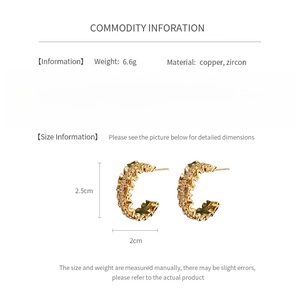 Detailed view of C-shaped golden earrings with wavy texture and zircon inlay details
