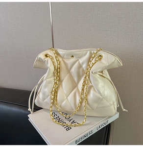 Detail of white quilted bucket bag with gold chain strap on decorative books