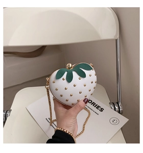 Close-up of white strawberry shaped mini bag with green leaves and gold chain strap