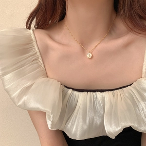 Close-up of a gold necklace featuring a white mother-of-pearl rose pendant on a model