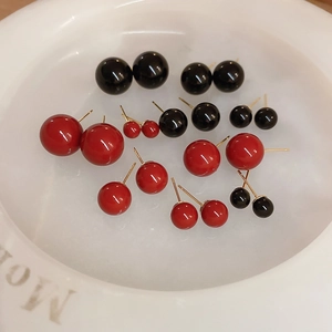 Macro detail of red and black spherical stud earrings in various sizes inside a white bowl
