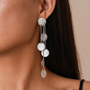 Close-up of long silver tassel earrings with round textured pendants on a model