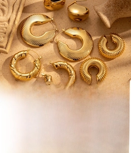 Detail of gold titanium steel hoop earrings on a textured stone background
