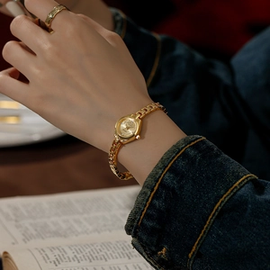 Elegant gold quartz watch with a small round dial and chain strap on female wrist