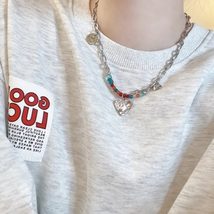 Détail d'un collier cœur argenté avec perles colorées et breloques étoile sur sweat gris