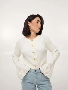 Close-up of white ribbed knit cardigan featuring decorative gold embossed metal buttons