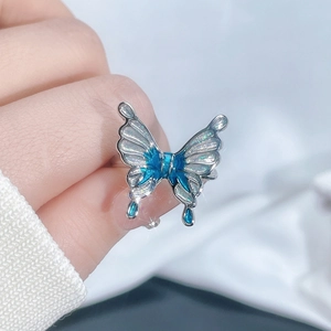 Close-up of irregular silver butterfly ring with blue enamel wings and teardrop charms