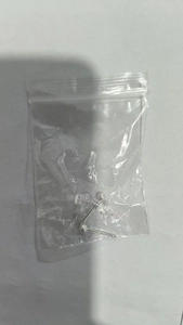Macro view of minimalist round silver stud earrings with plastic ear plugs in packaging
