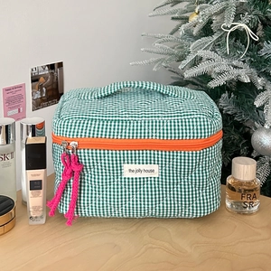 Detail of green and white checkered quilted makeup bag with vibrant orange zipper closure