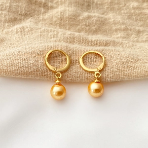 Detailed macro view of 18K gold-plated leverback earrings with lustrous golden pearls