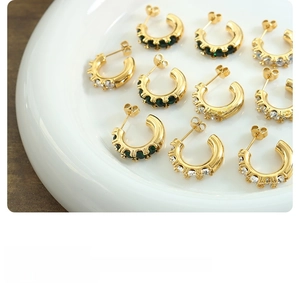 Détail de boucles d'oreilles créoles dorées avec zircons verts et blancs alternés