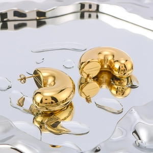 Polished 18K gold plated C-shaped chunky hoop earrings on reflective water surface