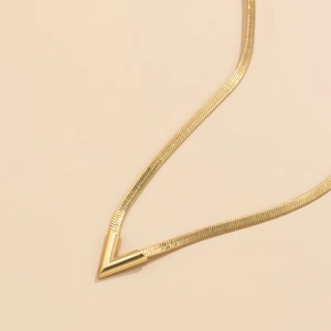 Detalle de un colgante en V dorado minimalista en una cadena de serpiente plana