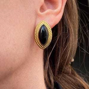 Close-up of gold-plated stud earring with black oval stone worn on a model's ear