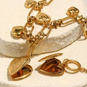 Detail of gold heart locket and pendant on white stone with polished cuban chain links