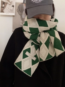 Détail d'une écharpe en maille à losanges verts et blancs avec étiquette minimaliste