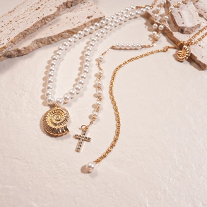 Macro detail of pearl necklace with gold conch shell and rhinestone cross pendants