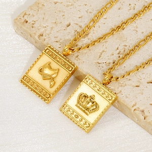 Close-up of golden Figaro chains with embossed heart and crown rectangular pendants