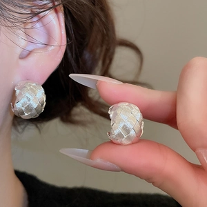 Close-up of silver C-shaped earrings with woven texture on model and in hand