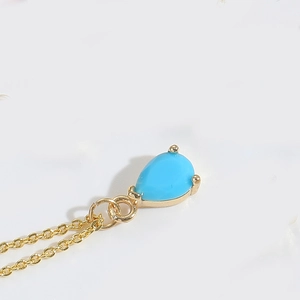 Macro view of blue teardrop crystal pendant in gold claw setting on a fine chain
