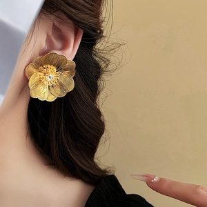 Detail of gold-plated hollow flower earring with crystal center worn by a model