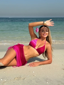 Three-piece hot pink crochet bikini set with mesh beach skirt on a sunny beach background