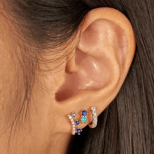 Macro shot of silver crown earrings with blue and white zircon stones on model ear