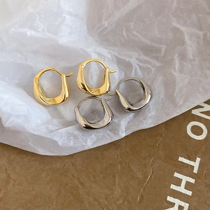Close-up of minimalist gold and silver U-shaped hoop earrings on natural paper texture