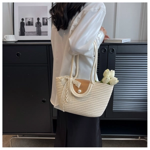 Detail of woven straw tote bag with brown leather flap, pearl clasp, and lace ribbon