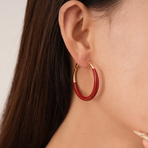 Detail shot of a large retro red enamel and gold hoop earring worn by a female model