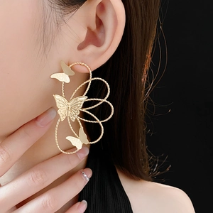 Close-up of golden hollow butterfly earrings worn by a model against a black background
