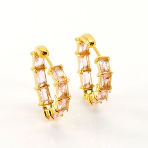 Gros plan de boucles d'oreilles créoles dorées avec zircons roses et boucle de ceinture