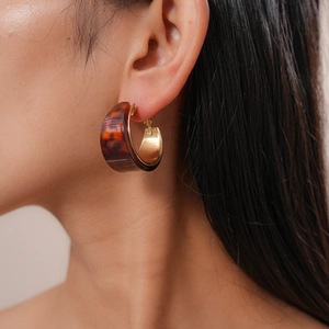 Close-up of model wearing thick C-shaped tortoise shell resin hoop earrings with gold metal