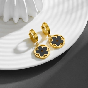 Boucles d'oreilles trèfle dorées avec émail noir sur une assiette en céramique