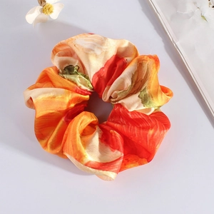Detailed view of an orange oil painting floral satin scrunchie with a silky texture