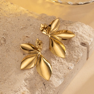 Close-up of golden leaf-shaped earrings with a polished finish on a light stone surface