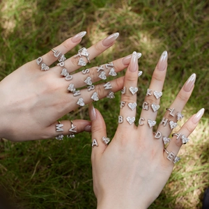 Close-up of S925 silver letter rings with heart-shaped zircon stones on female hands