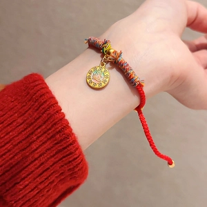 Gros plan du bracelet en corde tressée rouge avec un pendentif pièce dorée et soie colorée