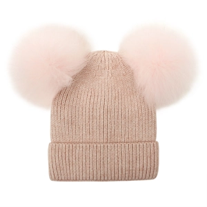 Detail of light pink knitted winter hat with two soft and large fluffy faux fur pom poms