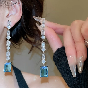 Detailed view of silver zircon tassel earrings featuring square emerald cut teal gemstones