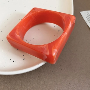 Detailed macro view of square acrylic bangle in bright orange-red with marbled texture