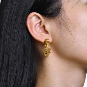 Detailed close-up of golden C-shaped twisted mesh hoop earrings worn on model