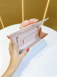 Detailed view of elegant pink evening clutch bag featuring a delicate floral decoration and silver chain.