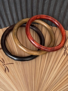 Gros plan de trois bracelets en bois poli en marron, jaune et rouge sur un éventail en bambou