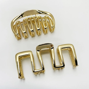 Detail view of two gold metal hair claws in semi-circle and wavy rectangular designs