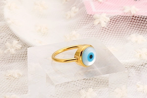 Close-up of golden evil eye ring on lace fabric, showing blue stone and metal details