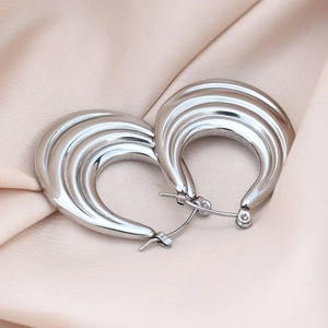 Detailed view of silver triple-layered hollow earrings on a beige silk fabric background