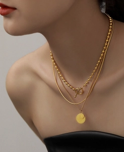 Close-up of triple-layered gold necklaces featuring a coin pendant and OT toggle clasp