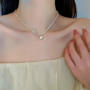 Detail of silver heart pendant necklace with pearl stitching on model's neck